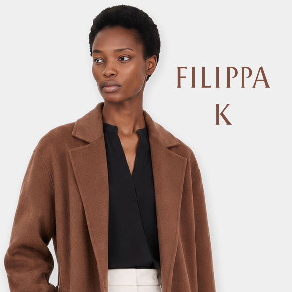 Eine Frau mit dunkler Hautfarbe in schwarzem Oberteil und braunem Mantel von Filippa K.